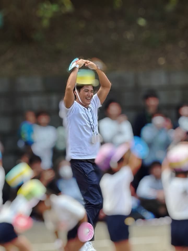 運動会でカラフルな帽子を頭に載せ、笑顔で両手を上げる男性