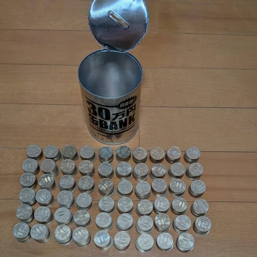 開いた缶とその前に並べて置いた大量の500円玉