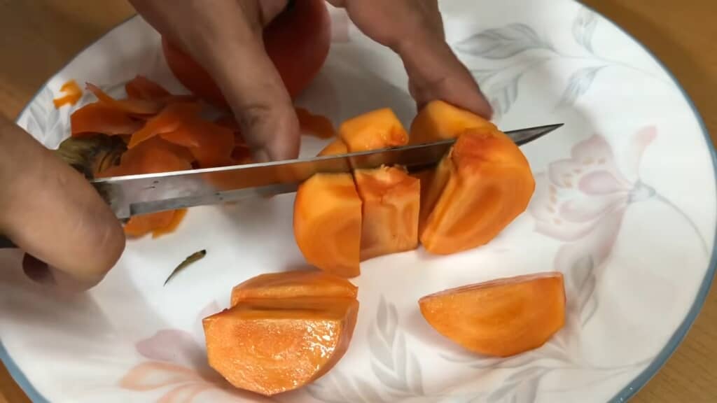 皮をむいた柿を包丁で食べやすい大きさに切り分ける様子