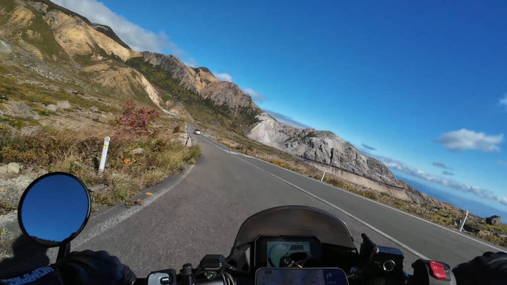 火山の荒々しい山肌を眺めながら山岳道路を走るバイク