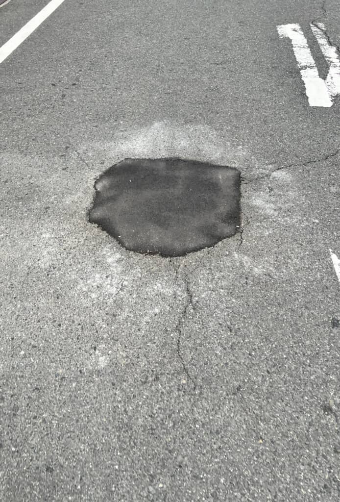 アスファルト舗装の道路で、破損箇所が黒い舗装材によって補修された様子